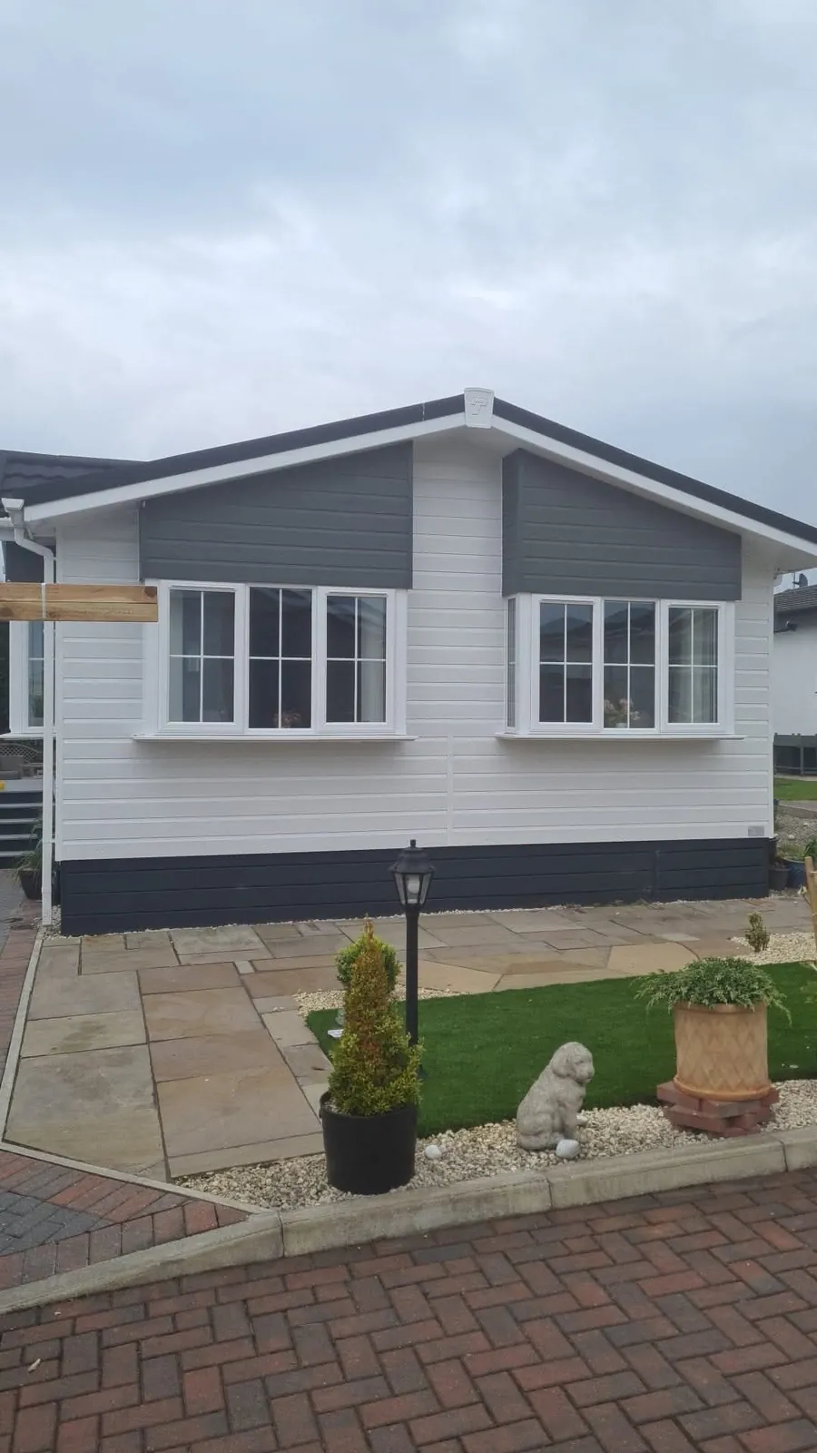 Single-storey bungalow with white and grey cladding and a new dark tiled roof, with paving and a small lawn in front