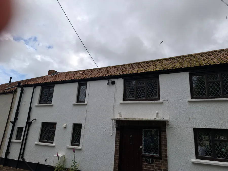 Two-storey rendered cottage with a mossy pantile roof and leaded windows, photographed during a roof survey
