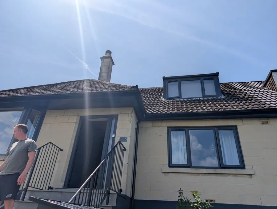 Front of a stone bungalow with a tiled roof, a new dormer window and a rendered chimney stack, photographed on a bright day