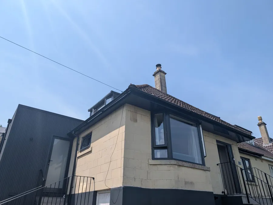 Dormer window set into a hipped tiled roof with a chimney stack and new black fascia and guttering on a rendered house in Newcastle