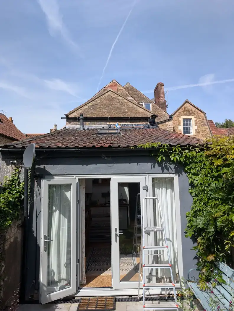 Small rear extension with a tiled lean-to roof and a new rooflight, with French doors open and a stepladder outside