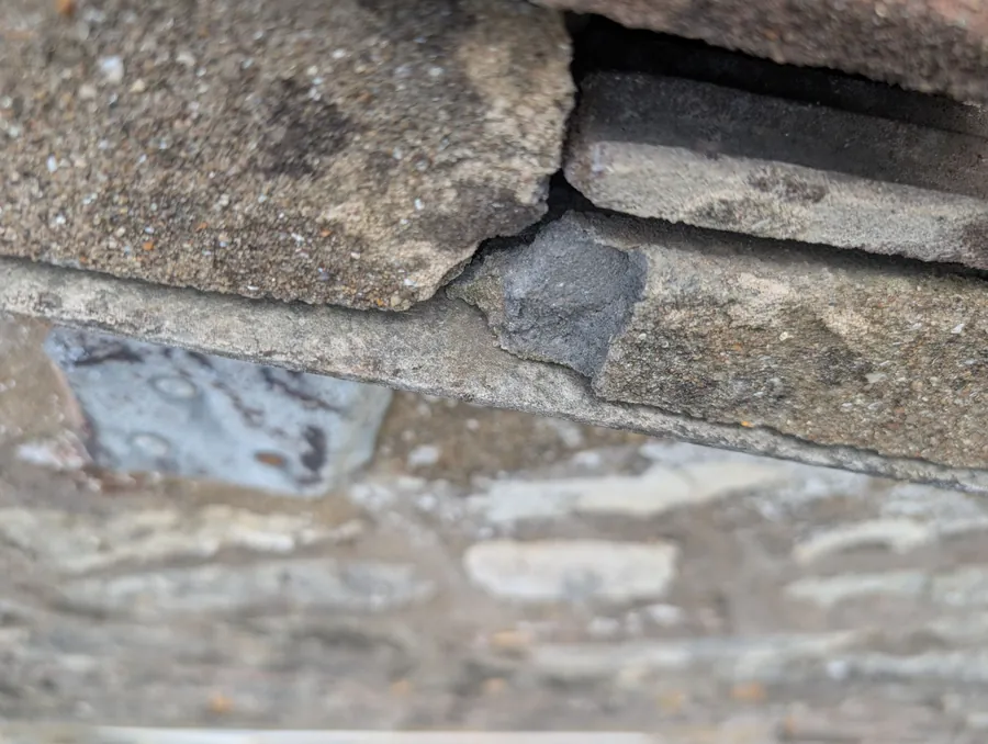 Broken mortar flashing with a gap open to the roof timbers at a wall abutment