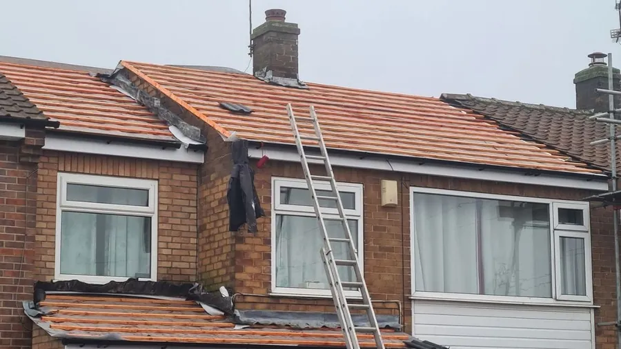 Semi-detached house in Newcastle mid re-roof with new battens fixed over membrane on the main roof and bay, a ladder up to the slope and the chimney stack behind