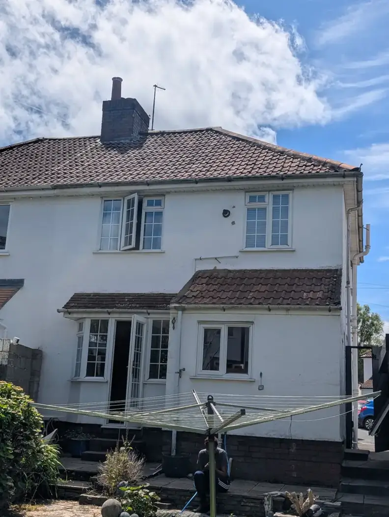 Rear of a white rendered semi-detached house with a brown tiled roof, small tiled canopies and a brick chimney stack